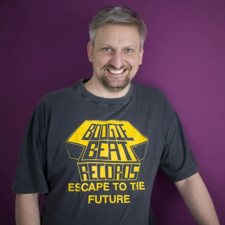Dash lächelnd im T-Shirt von Boogie Beat Records vor einer lila Wand